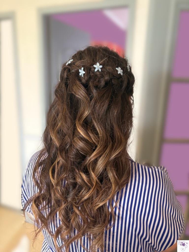 Vue arrière d'une coiffure semi-attachée composée de longues boucles ondulées et de tresses délicates ornées de petites fleurs blanches.