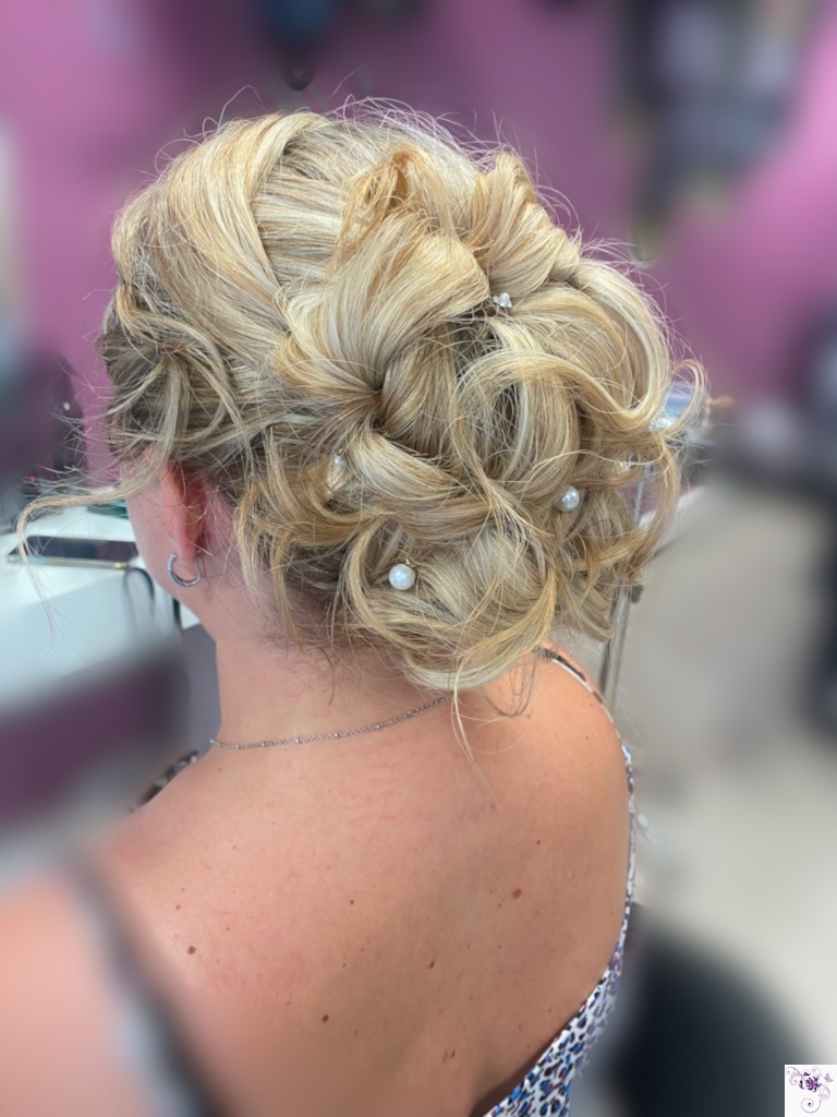 Vue arrière d'un chignon blond volumineux composé de boucles entrelacées et orné de plusieurs perles blanches réparties dans la coiffure.